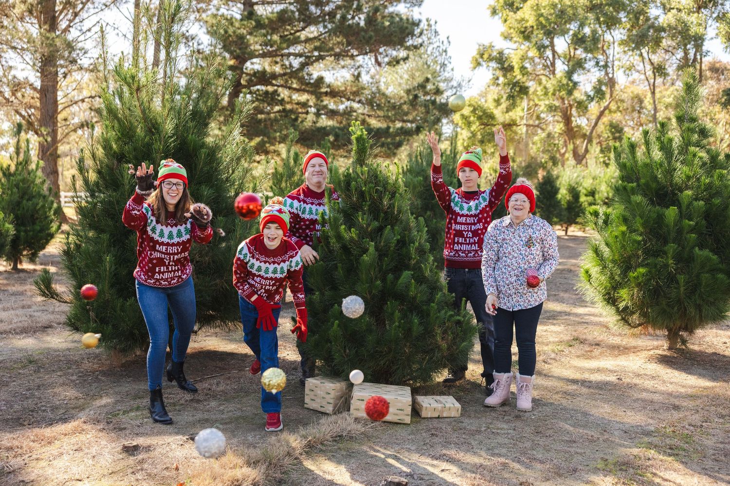Holiday family photoshoot in a Christmas tree farm with red and white coordinated outfits.