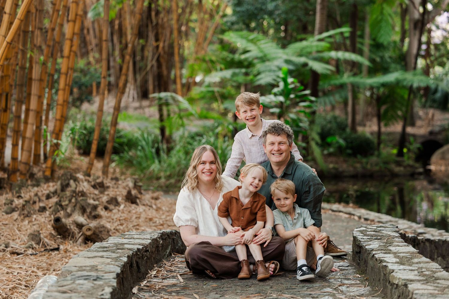 A group sits together on stone steps surrounded by lush bamboo and tropical foliage in an outdoor garden setting.
