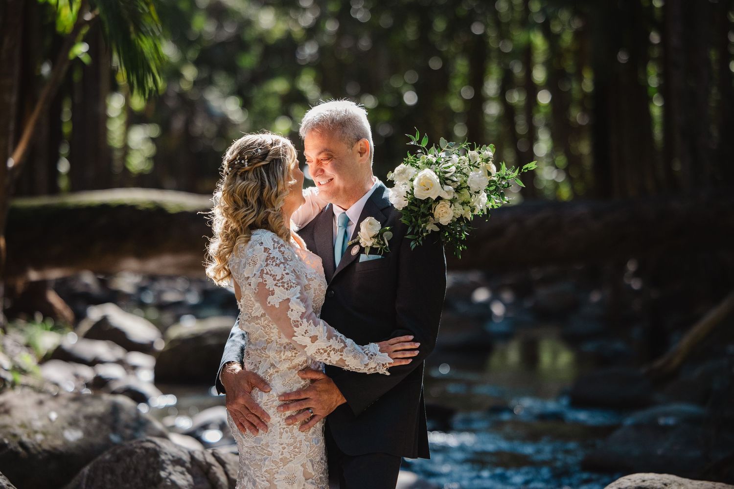 A couple shares an intimate moment during their wedding photoshoot in a lush outdoor forest setting.