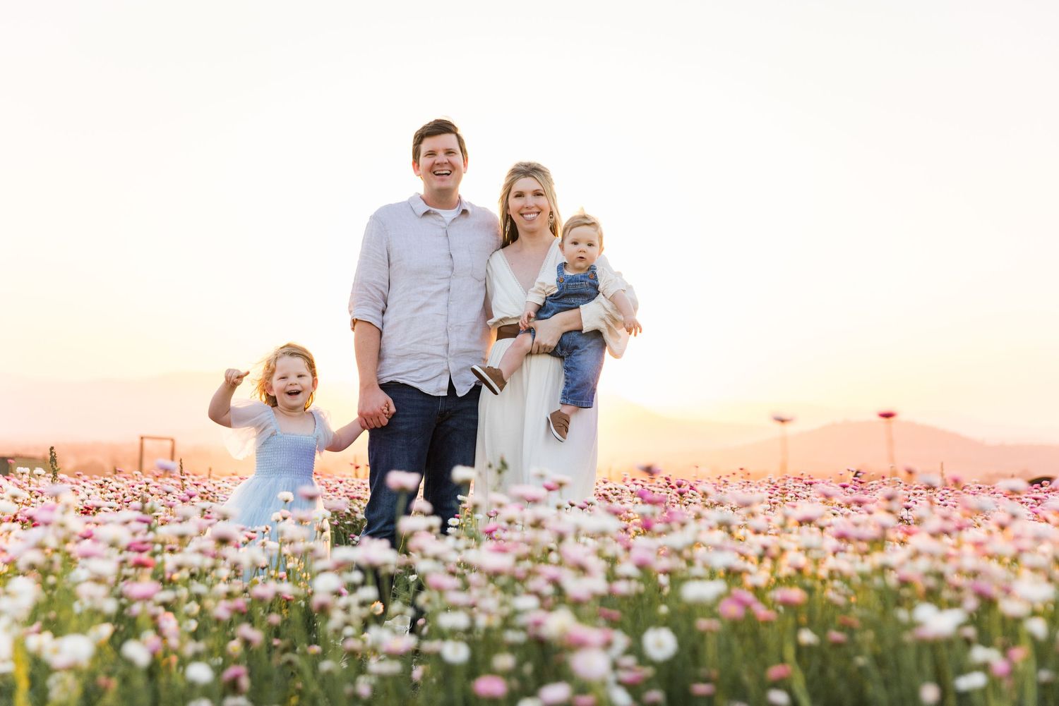 Family stands together in a beautiful field of pink and white cosmos flowers at sunset.