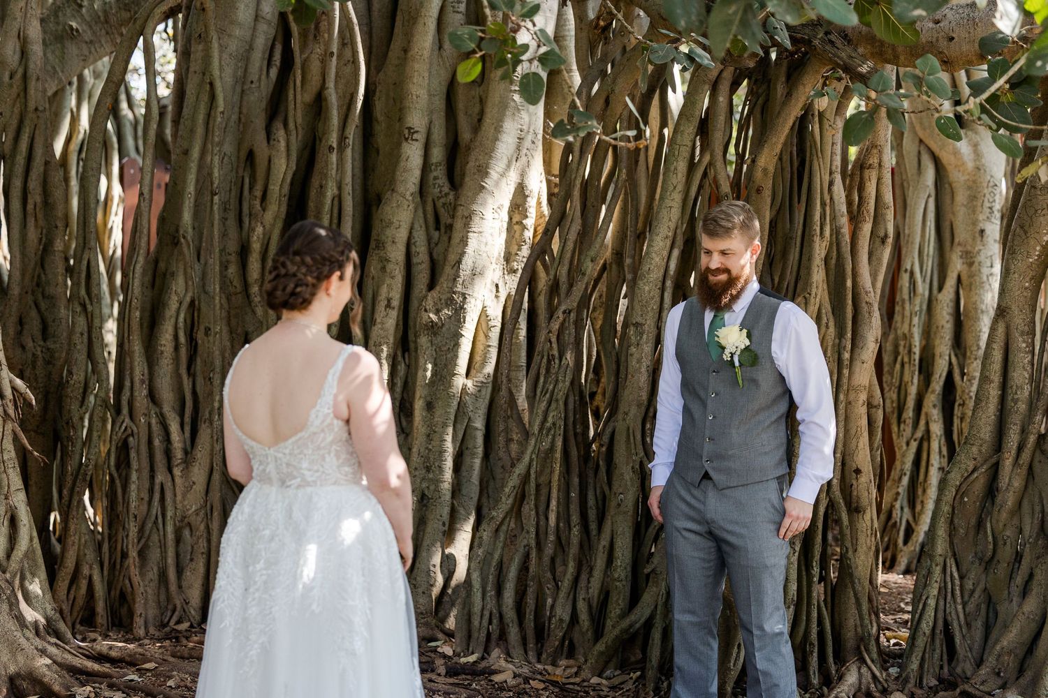 Bride and groom share a first look moment among dramatic banyan tree roots outdoors.