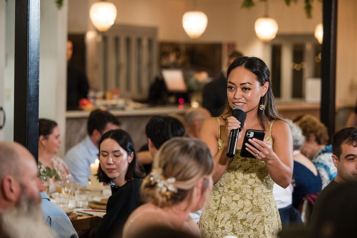 Woman in floral dress gives a speech with microphone at an elegant wedding reception dinner.