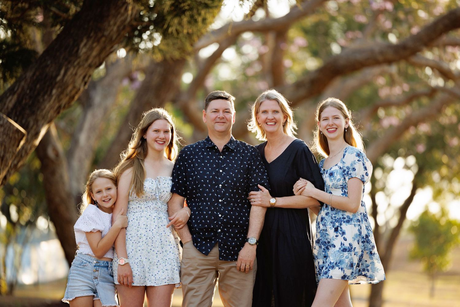 A family group walks together outdoors during golden hour in a natural setting with trees in the background.