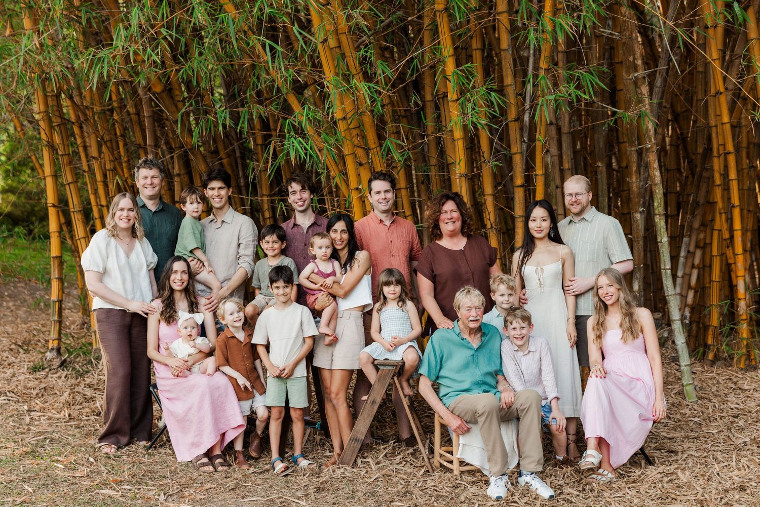 Group of people gathered in a bamboo forest wearing coordinated pastel and neutral colored outfits for outdoor photos.