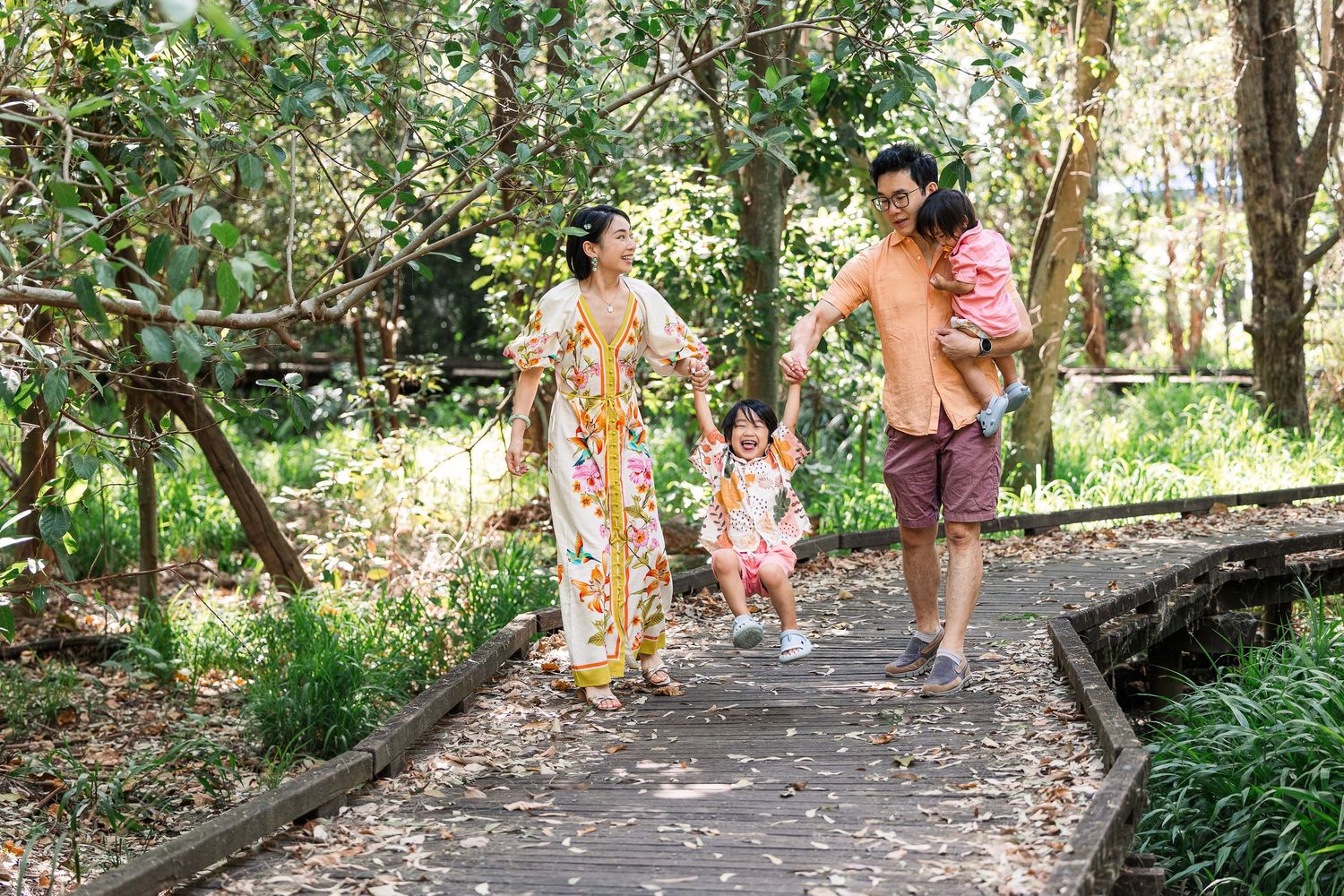 A family walks together on a winding forest path surrounded by lush greenery on a sunny day.