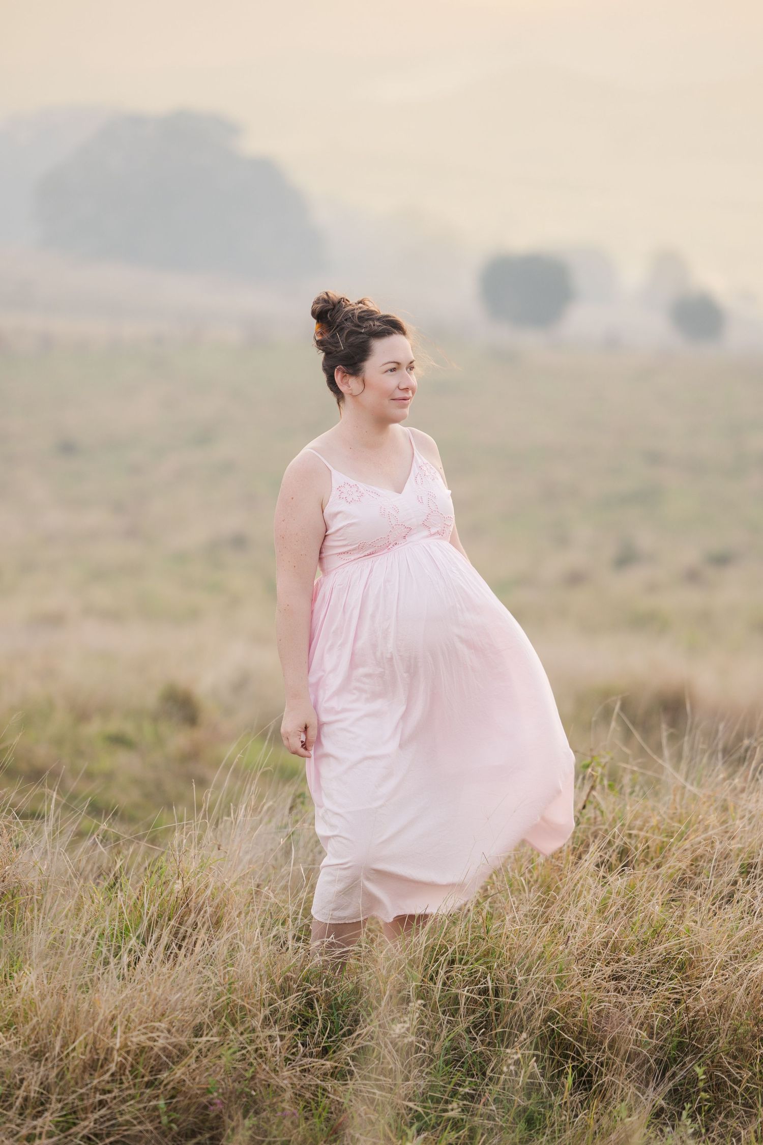 A person in a flowing pink dress twirls gracefully in a misty field of tall grass at sunrise.