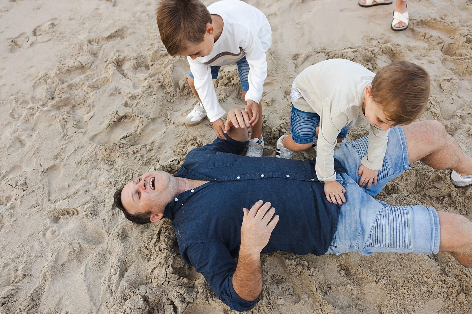 Kids playfully burying someone in the sand at the beach on a sunny day.