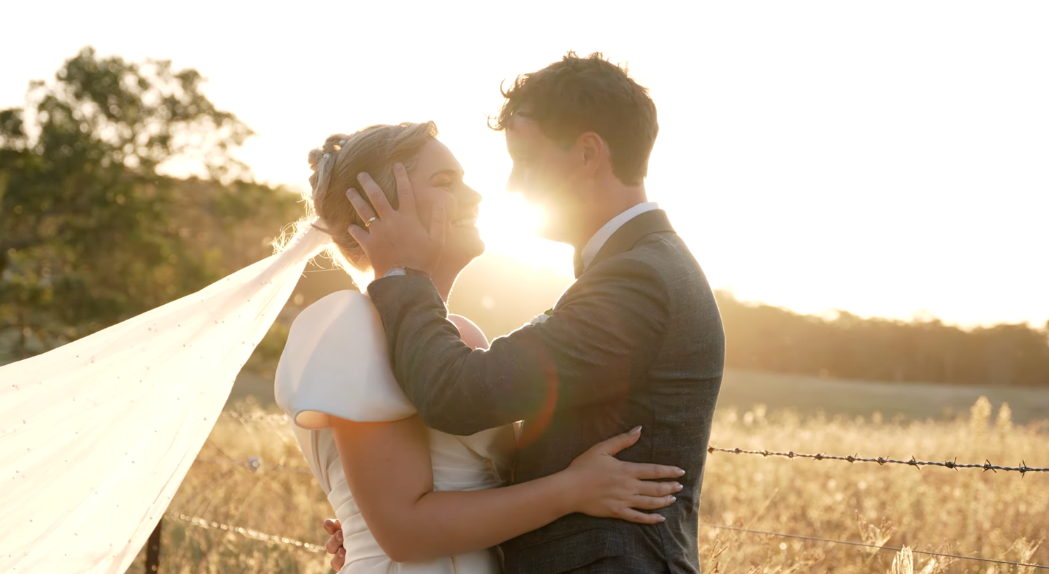 A couple embraces in a sunlit wheat field during golden hour while sharing a romantic moment.