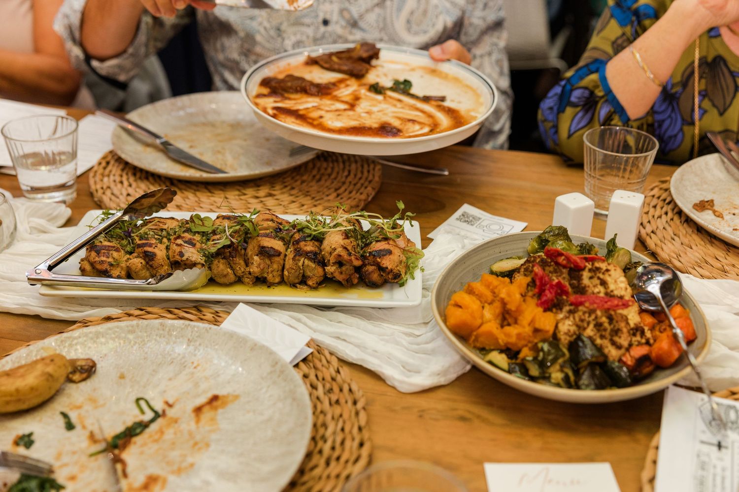A spread of Middle Eastern dishes including kebabs, hummus, and roasted vegetables served on a wooden table.