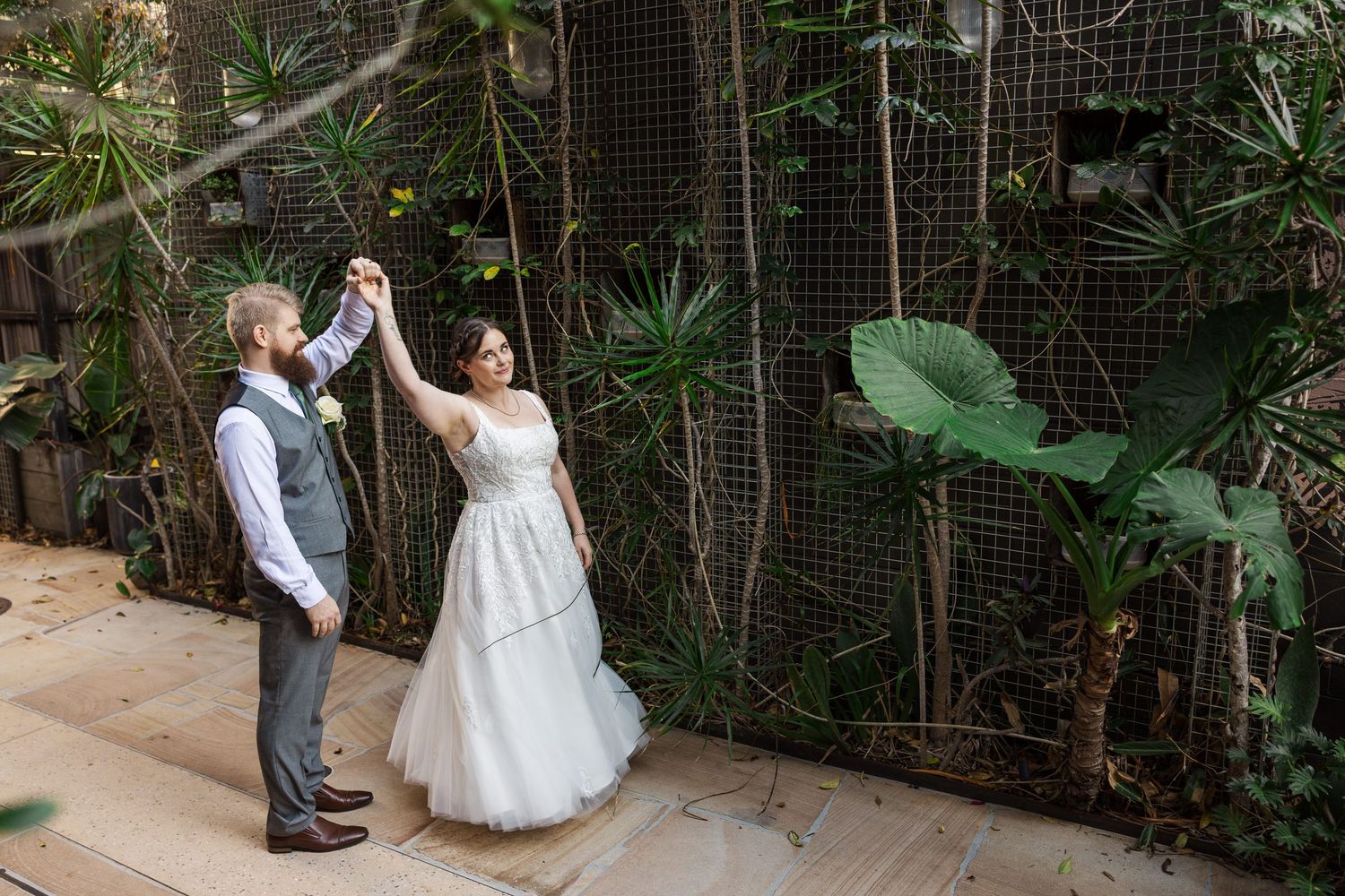Bride and groom share a romantic dance outdoors surrounded by lush tropical greenery at their wedding venue.