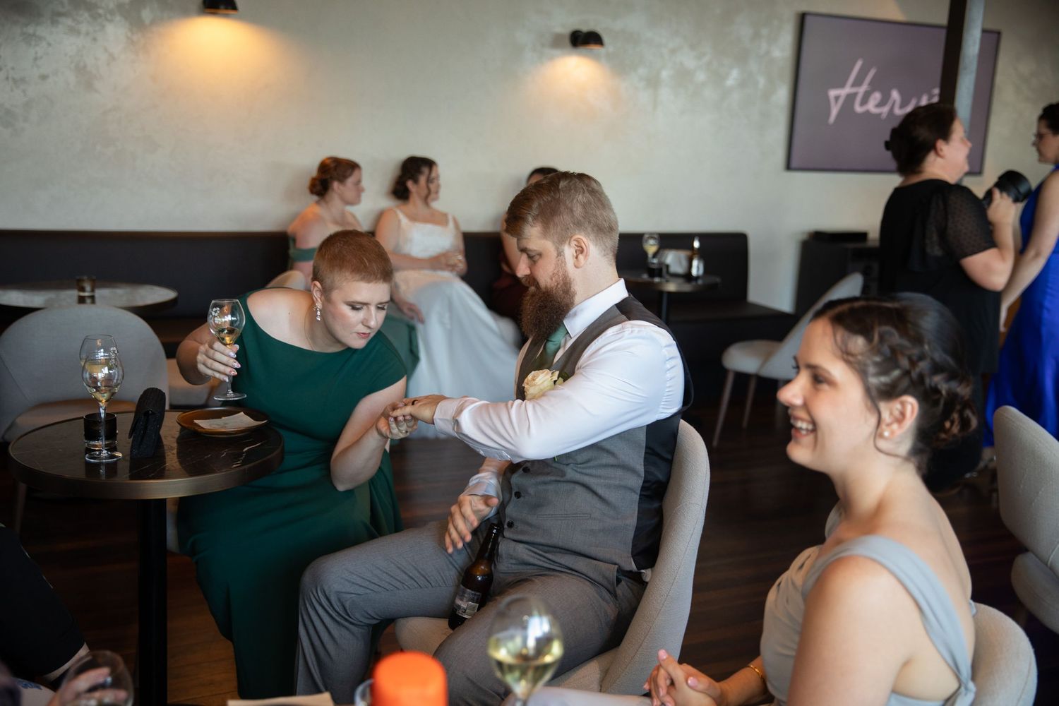 Wedding guests in formal attire socializing at a reception venue, with bridesmaids in blue dresses and a bearded groomsman.