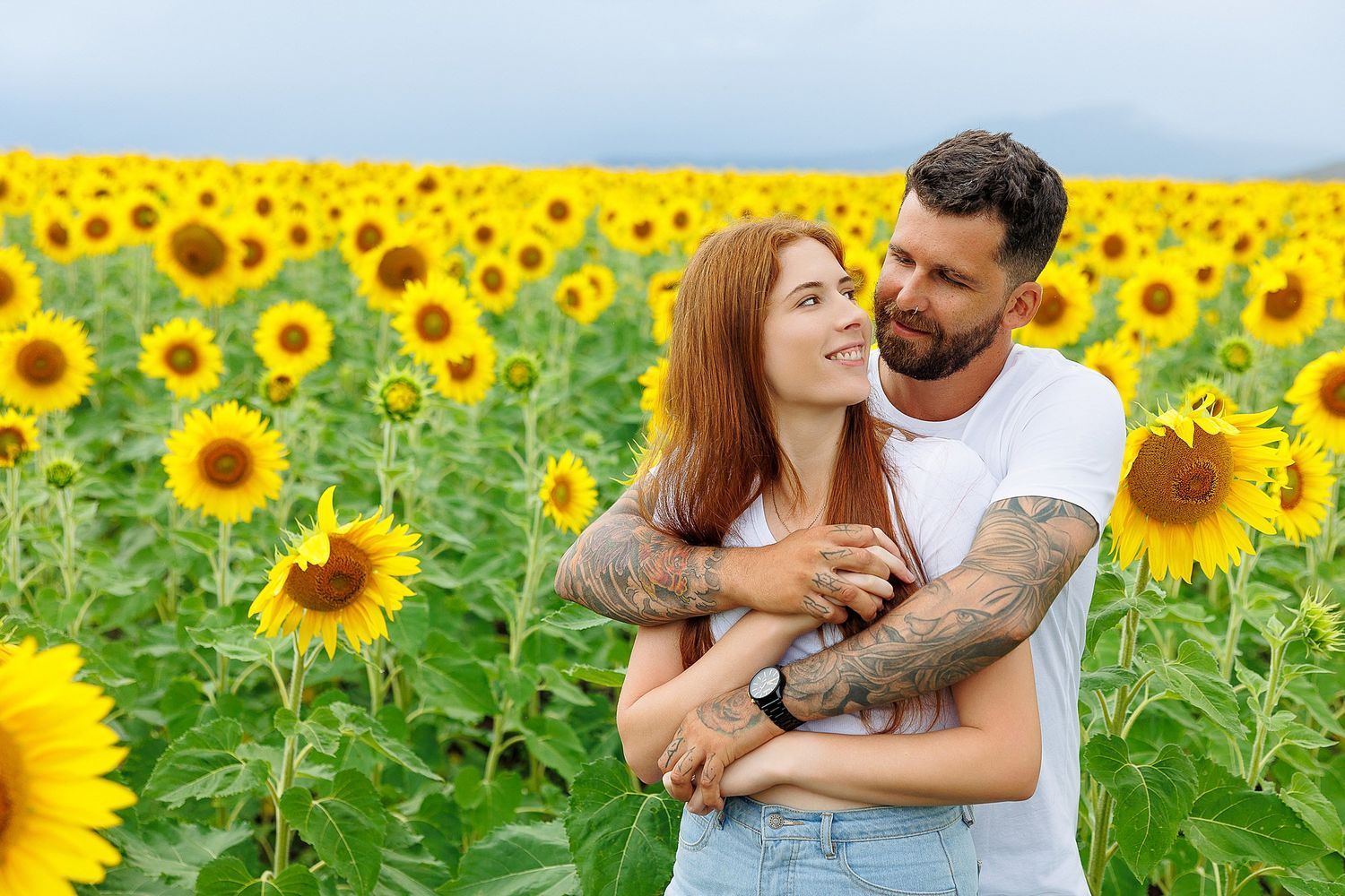 Loving couple sharing an intimate embrace in a vibrant yellow sunflower field on a bright sunny day.