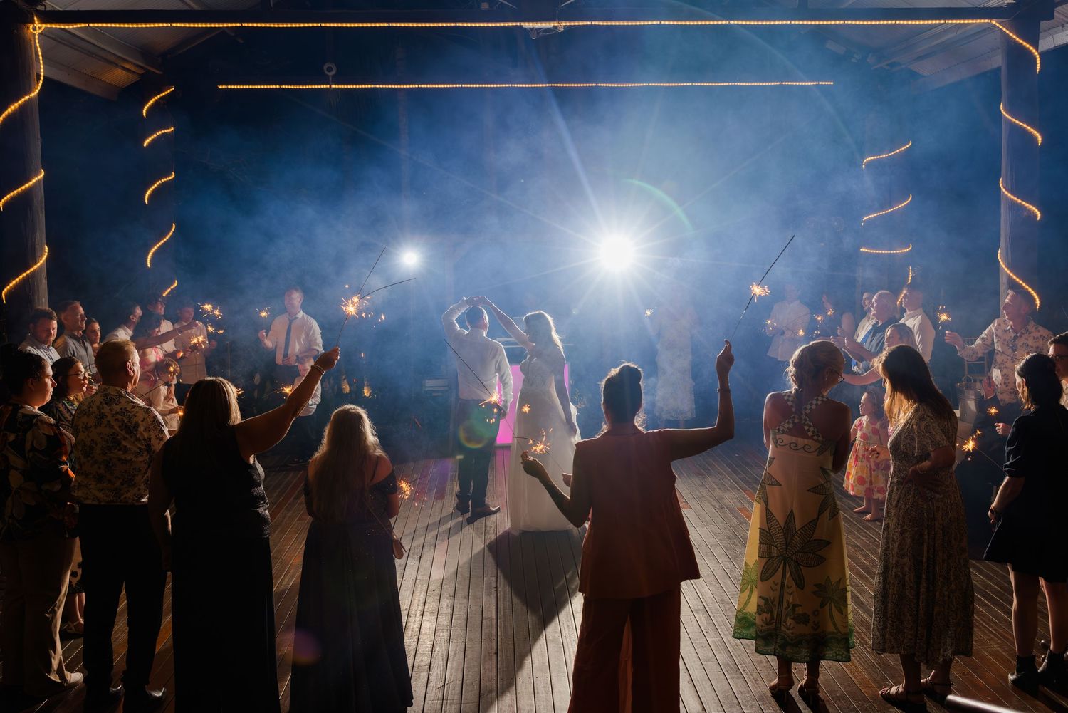 Silhouettes of wedding guests dancing under dramatic blue lighting at an indoor reception venue.