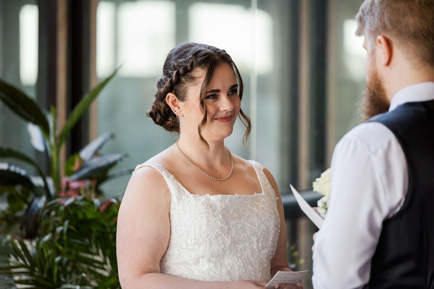 Bride smiling warmly at groom during wedding ceremony in elegant white lace dress with updo hairstyle.