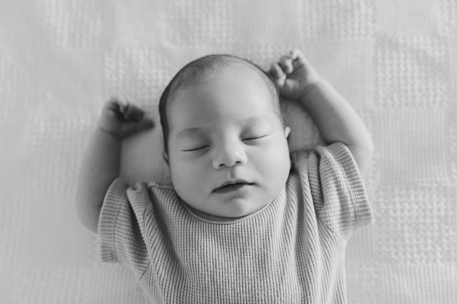 A series of four black and white photos showing a sleeping newborn baby in soft gray clothing.