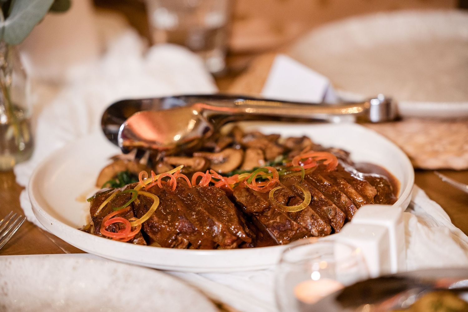 Glazed beef brisket topped with sautéed mushrooms and julienned carrots served on a white platter.