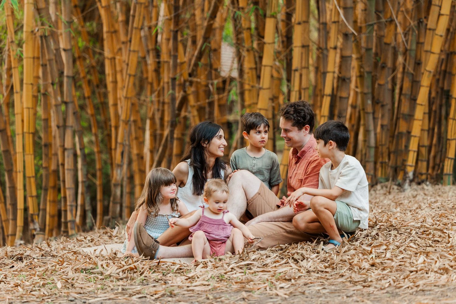 A family sits together on fallen autumn leaves in a golden forest during a fall photo session.