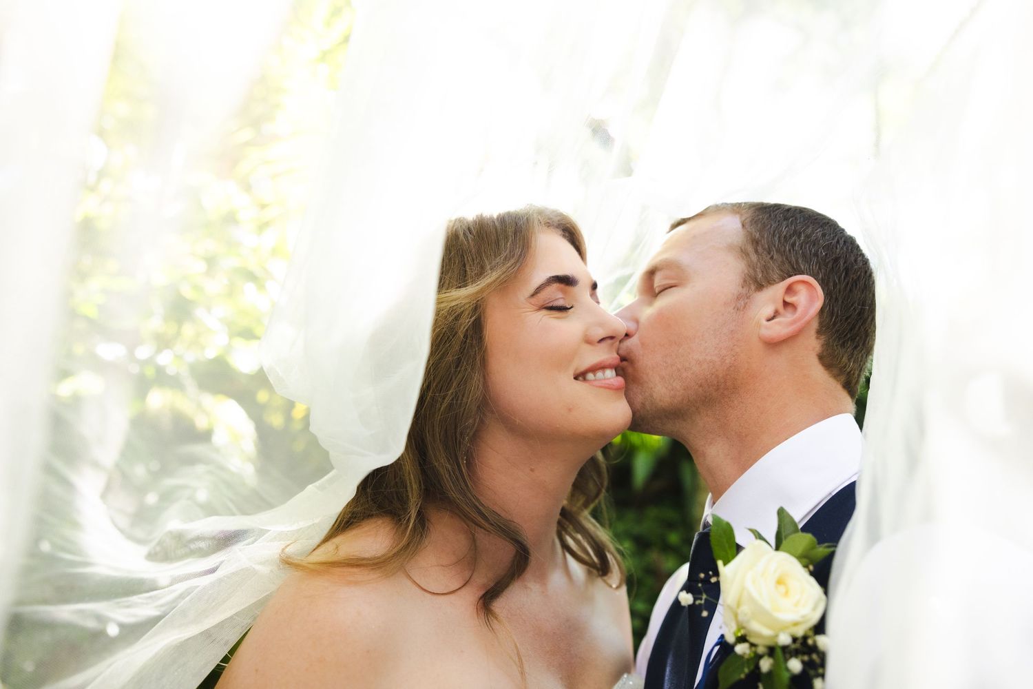 A couple shares a romantic kiss during their wedding ceremony with a beautiful outdoor backdrop.