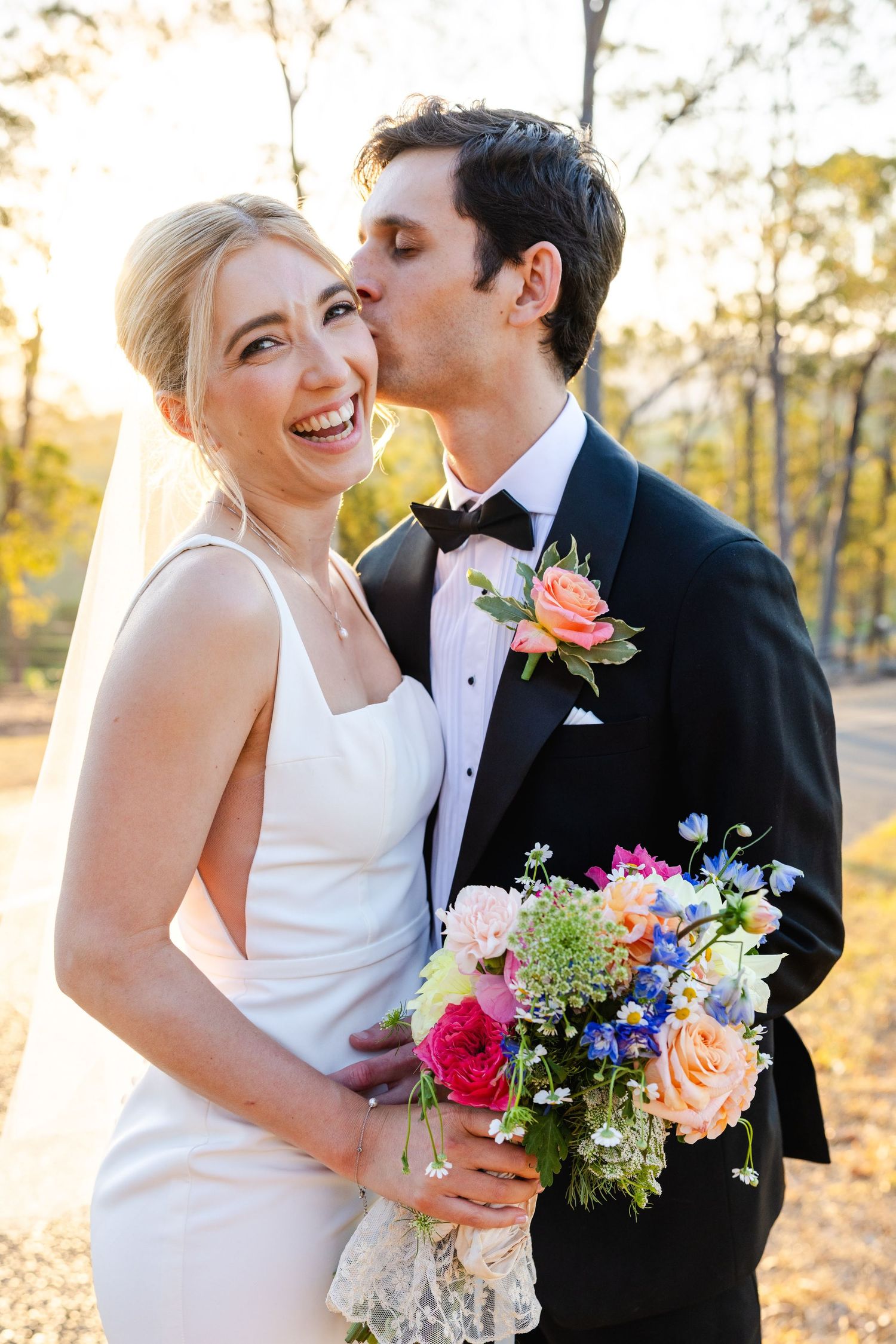 A joyful wedding moment captured outdoors with a vibrant bouquet featuring roses and wildflowers in autumn sunlight.