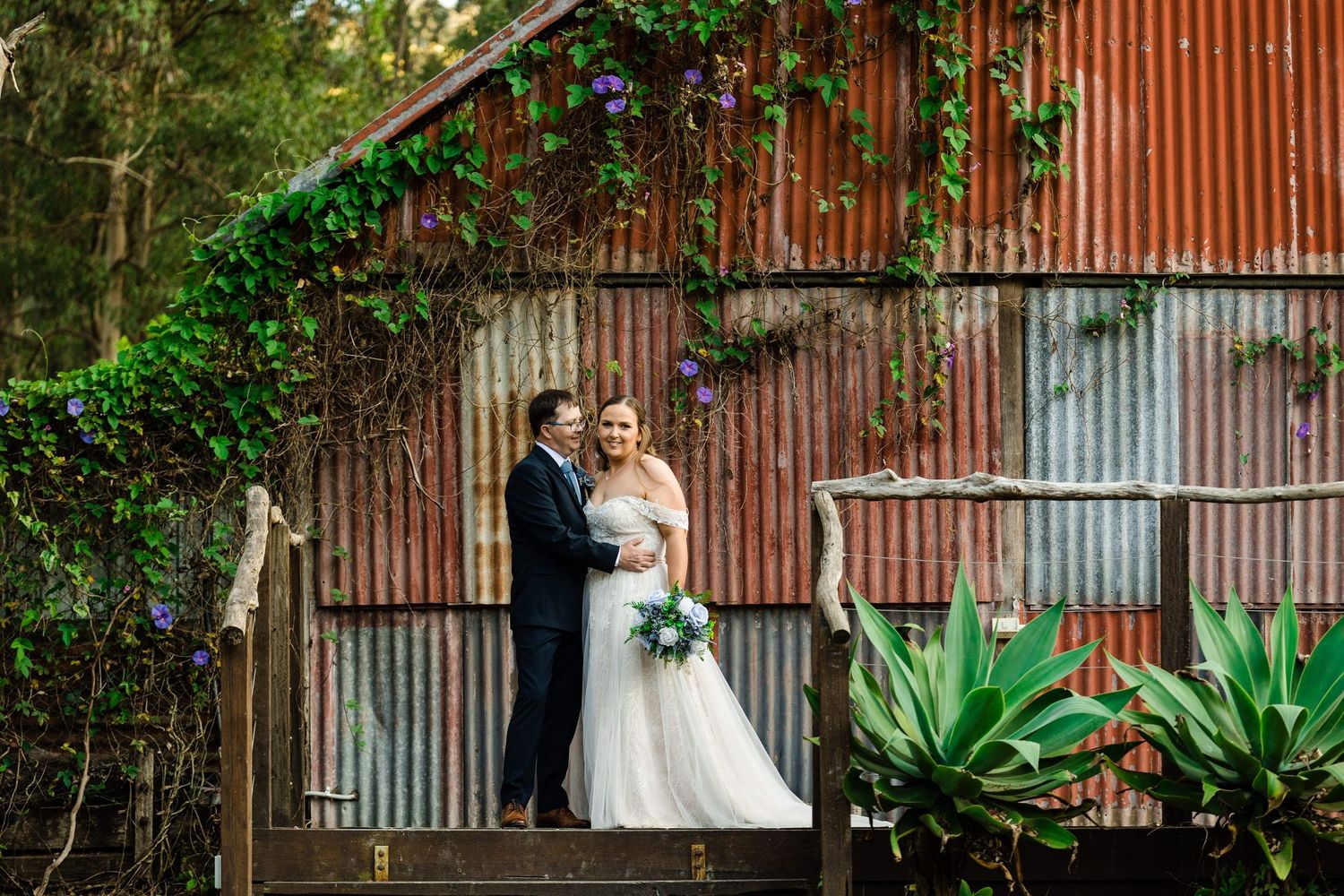 Romantic wedding photography series featuring a couple against a rustic red barn wall with lush greenery.
