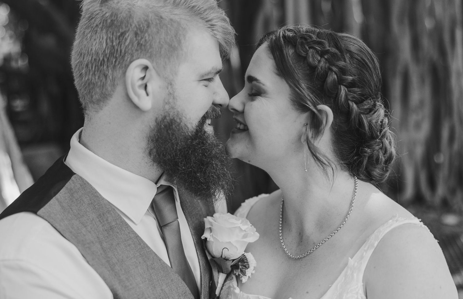 Black and white photo of a bearded groom and bride in a braid nearly kissing at their wedding ceremony.