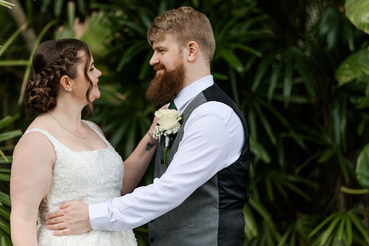 Bride adjusting groom's boutonniere in lush garden setting, sharing a tender moment on their wedding day.