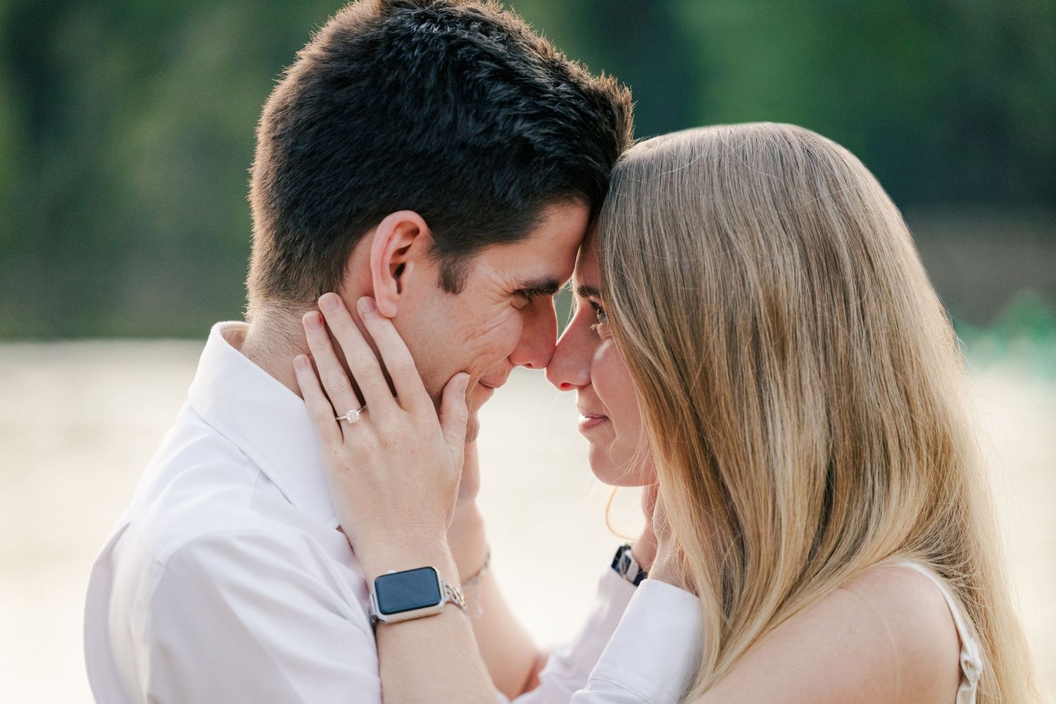 A couple in white clothing embraces tenderly in a romantic outdoor setting during a photo session.