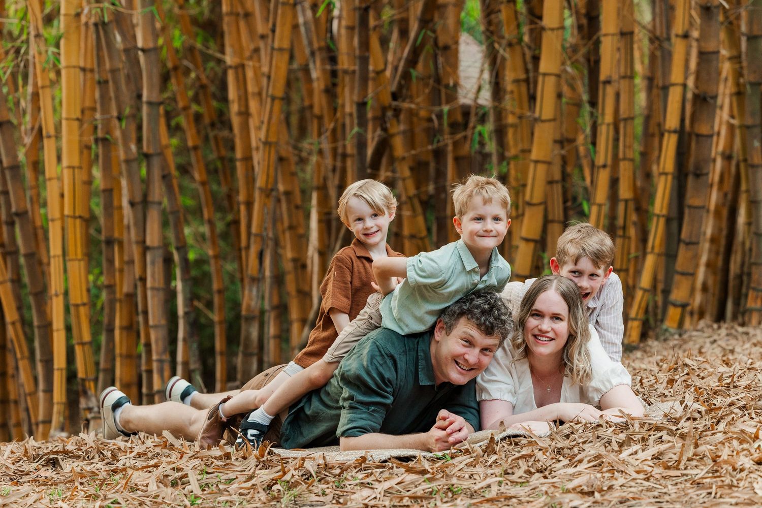 A group plays and poses together in autumn leaves against a backdrop of tall bamboo stalks in a forest setting.