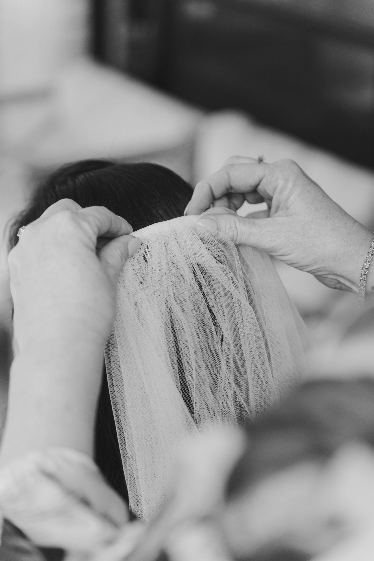 Hands delicately adjusting a white wedding veil in a black and white photograph.