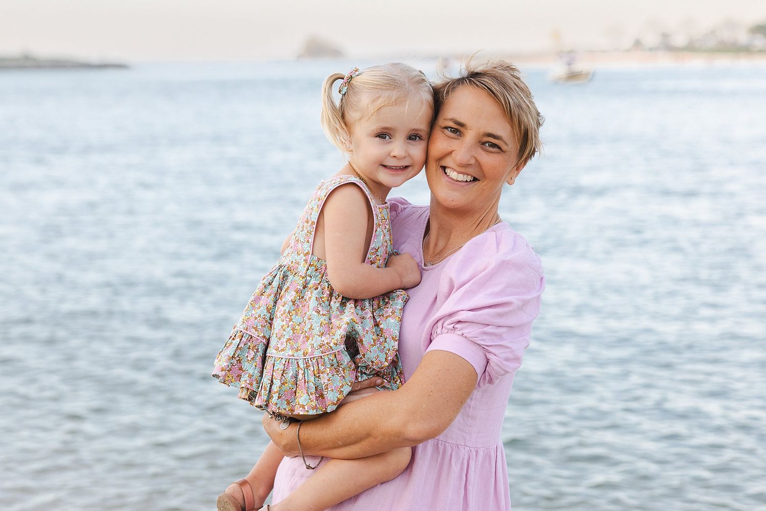 A tender moment shared between parent and child embracing by the ocean on a bright sunny day.