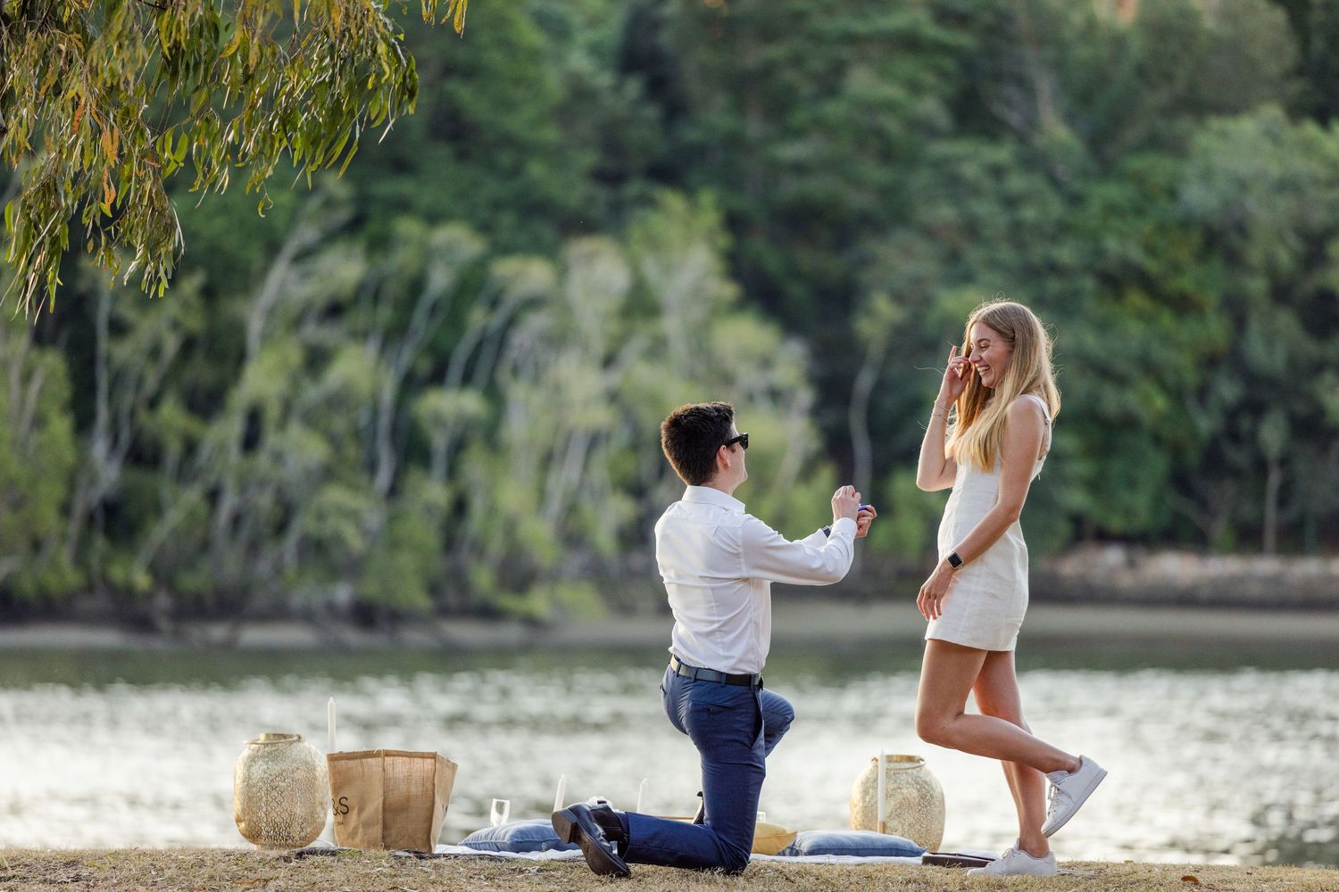 A couple walks along a scenic lakeside path surrounded by lush green trees and natural scenery.