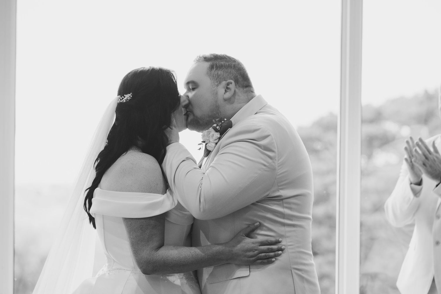 Black and white photo of a bride and groom sharing their first kiss at an outdoor wedding ceremony.