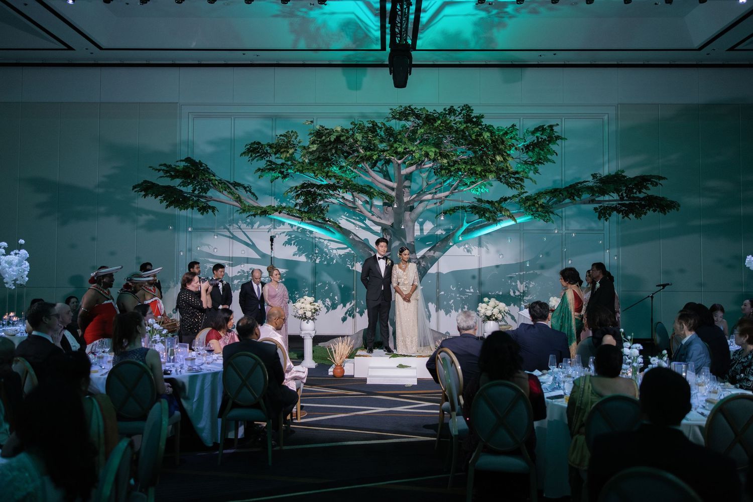 A wedding reception venue decorated with turquoise uplighting and white linens creates an elegant atmosphere.