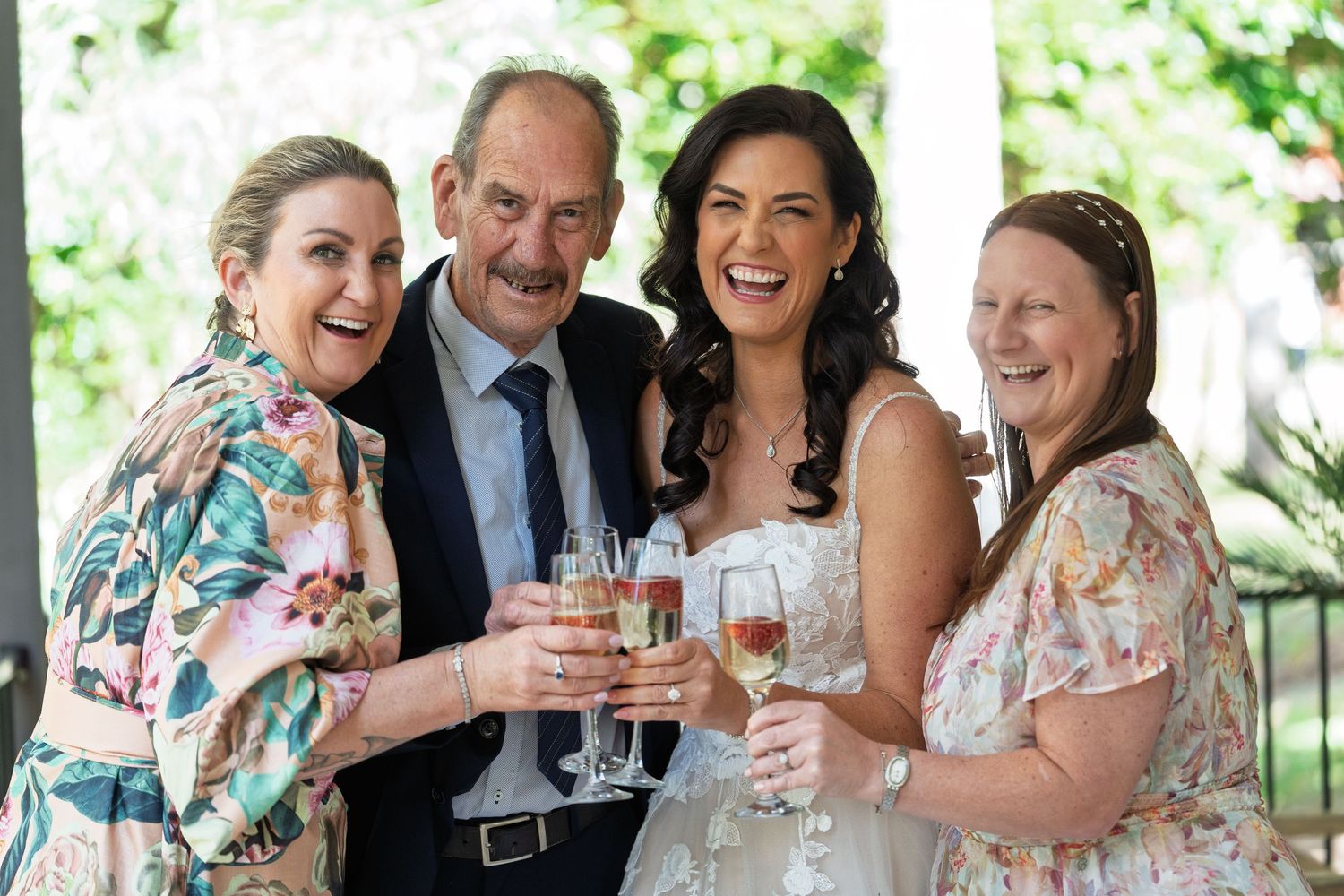 Wedding guests enjoying drinks and conversation at an outdoor reception under greenery.