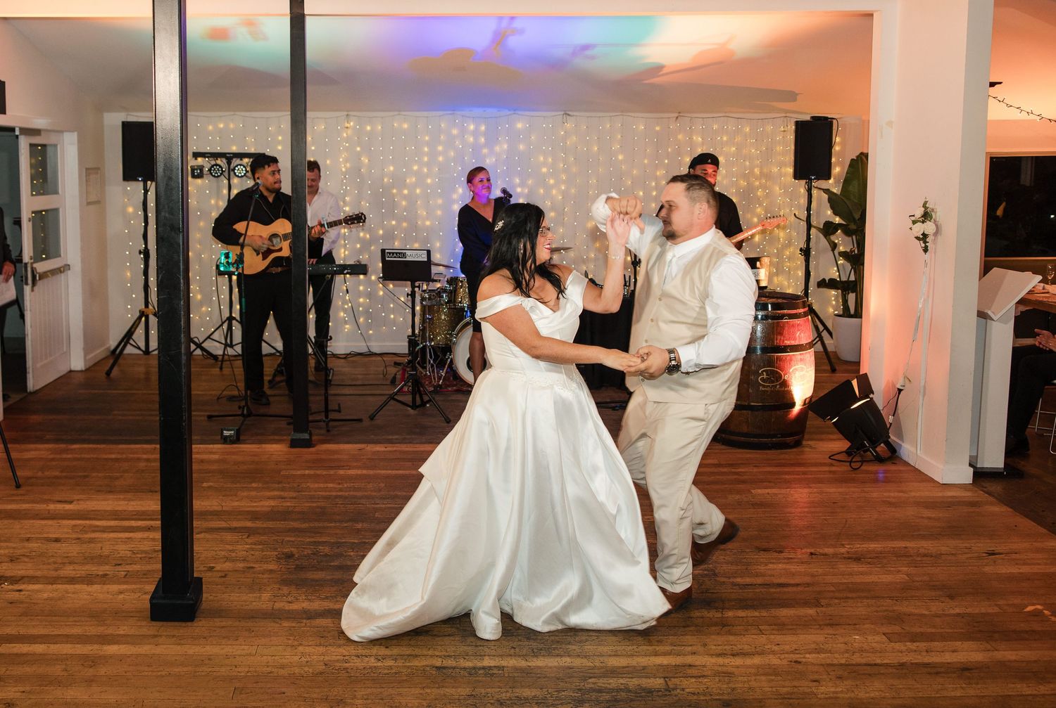Bride and groom share first dance at wedding reception with live band performing on stage in elegant venue.