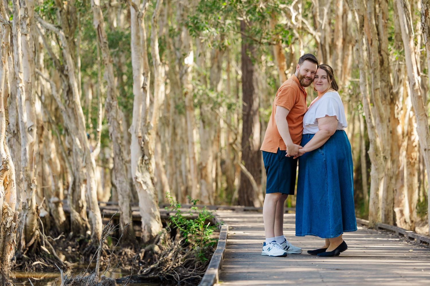 Two people stand together on a wooden boardwalk path through a scenic cypress swamp forest.