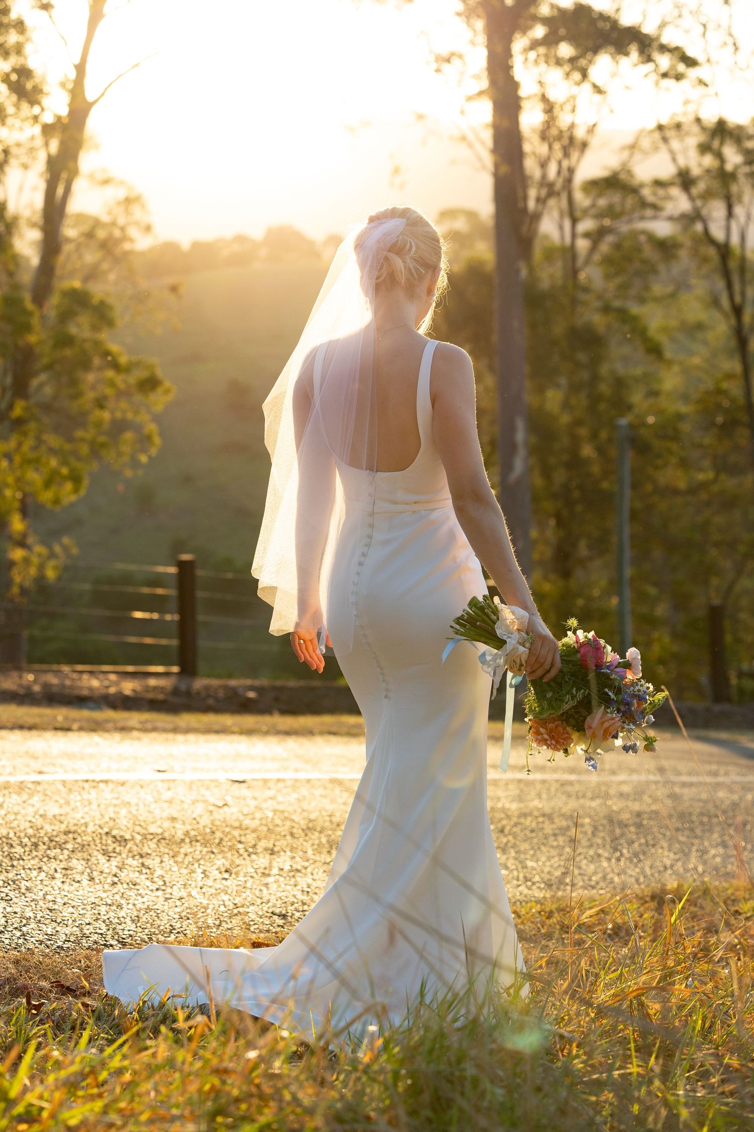 Wedding dress silhouettes against golden sunlight in a scenic countryside setting.
