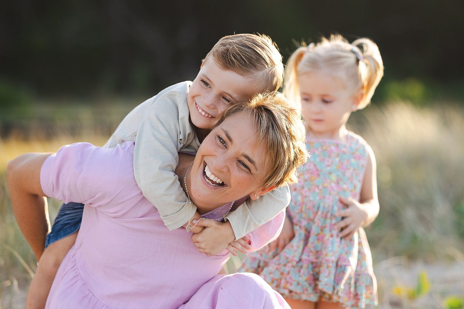 Three people having fun and playing together outdoors in a sunlit field with a natural blurred background.