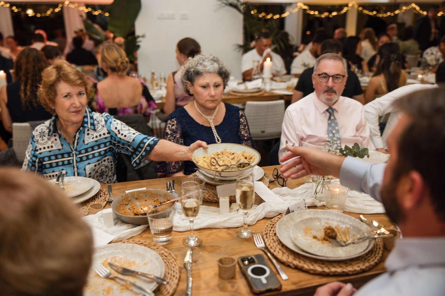 Guests sharing food at a elegantly set wedding reception dinner table with decorative centerpieces.