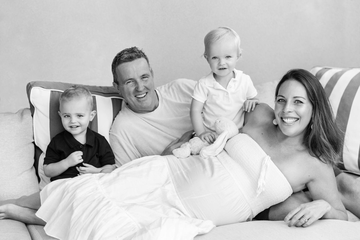 A black and white family portrait shows parents and children relaxing together on a couch, with a light, joyful mood.