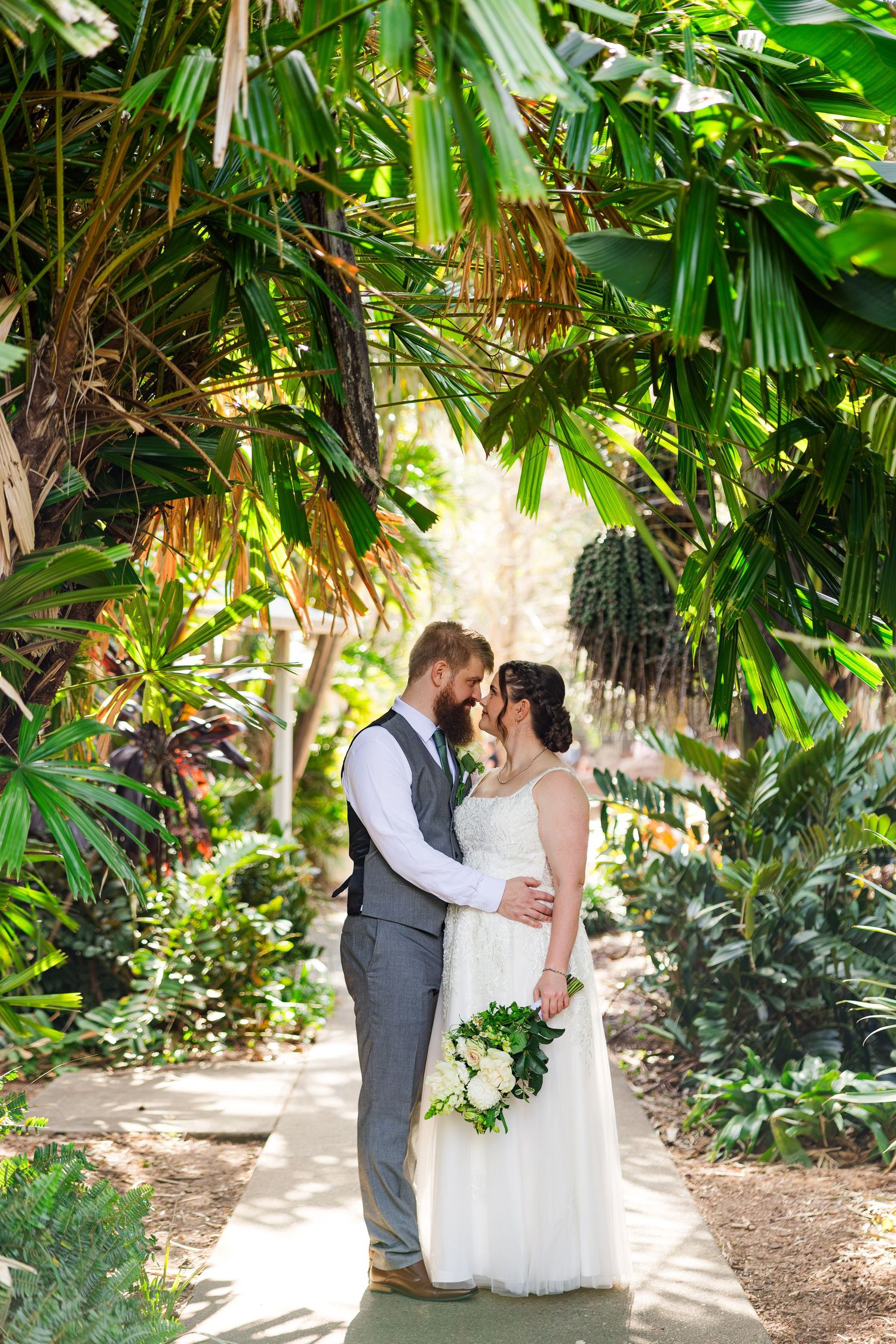 Bride and groom share a romantic moment surrounded by lush tropical greenery on their wedding day.