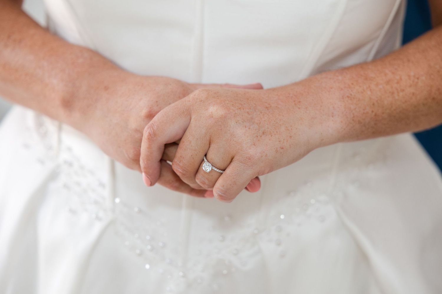 Close-up of a bride's hands clasped together, wearing a diamond engagement ring on her wedding day.