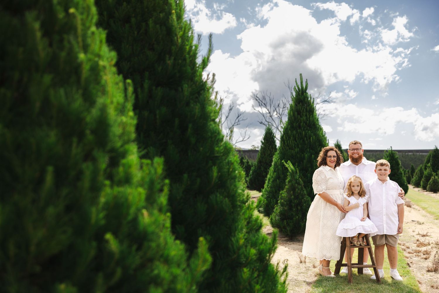 A couple poses for wedding photos in a lush green garden setting with dramatic cloudy skies overhead.