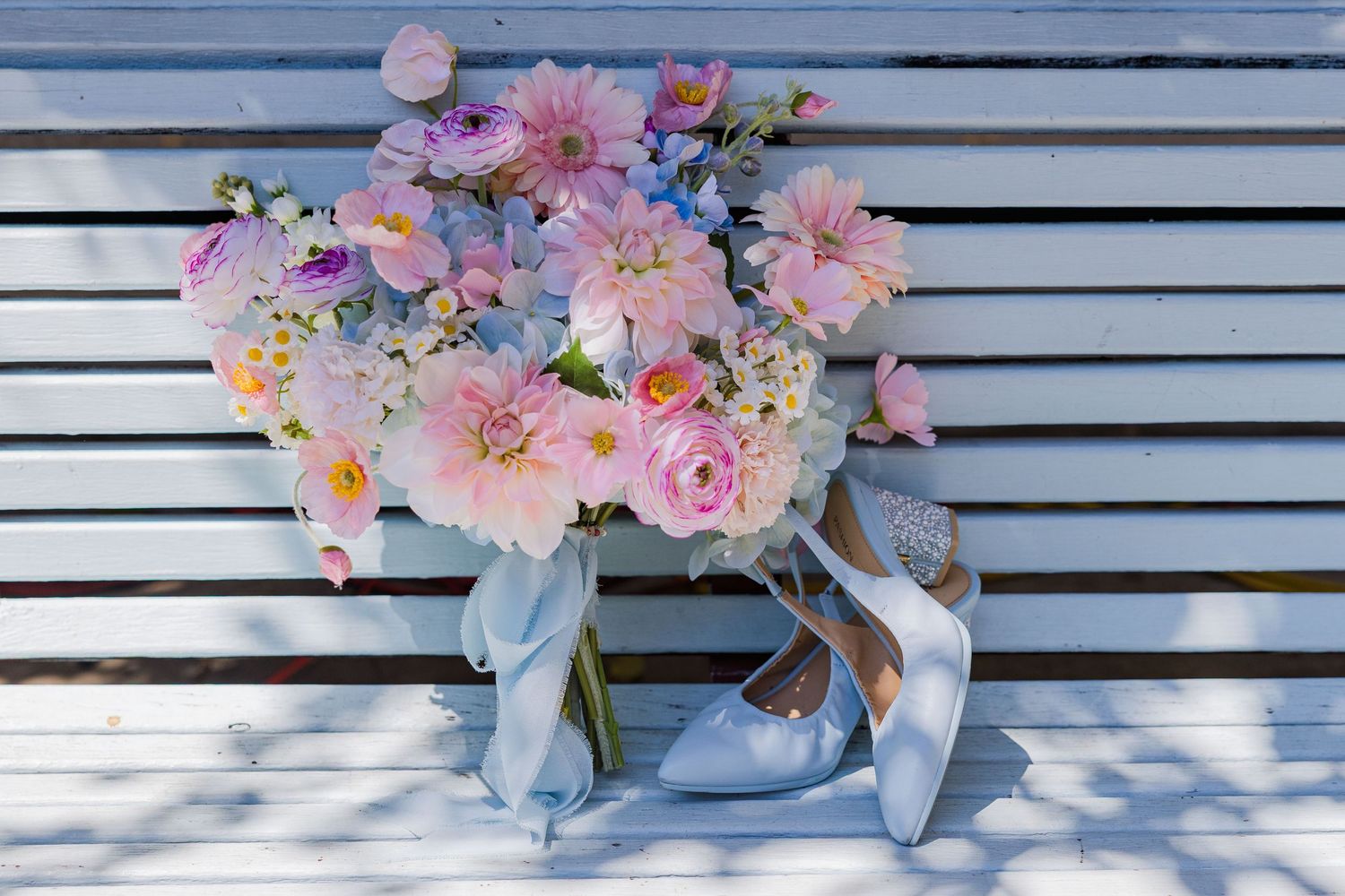Pink and white floral arrangements in light blue vases displayed against a white slatted backdrop.