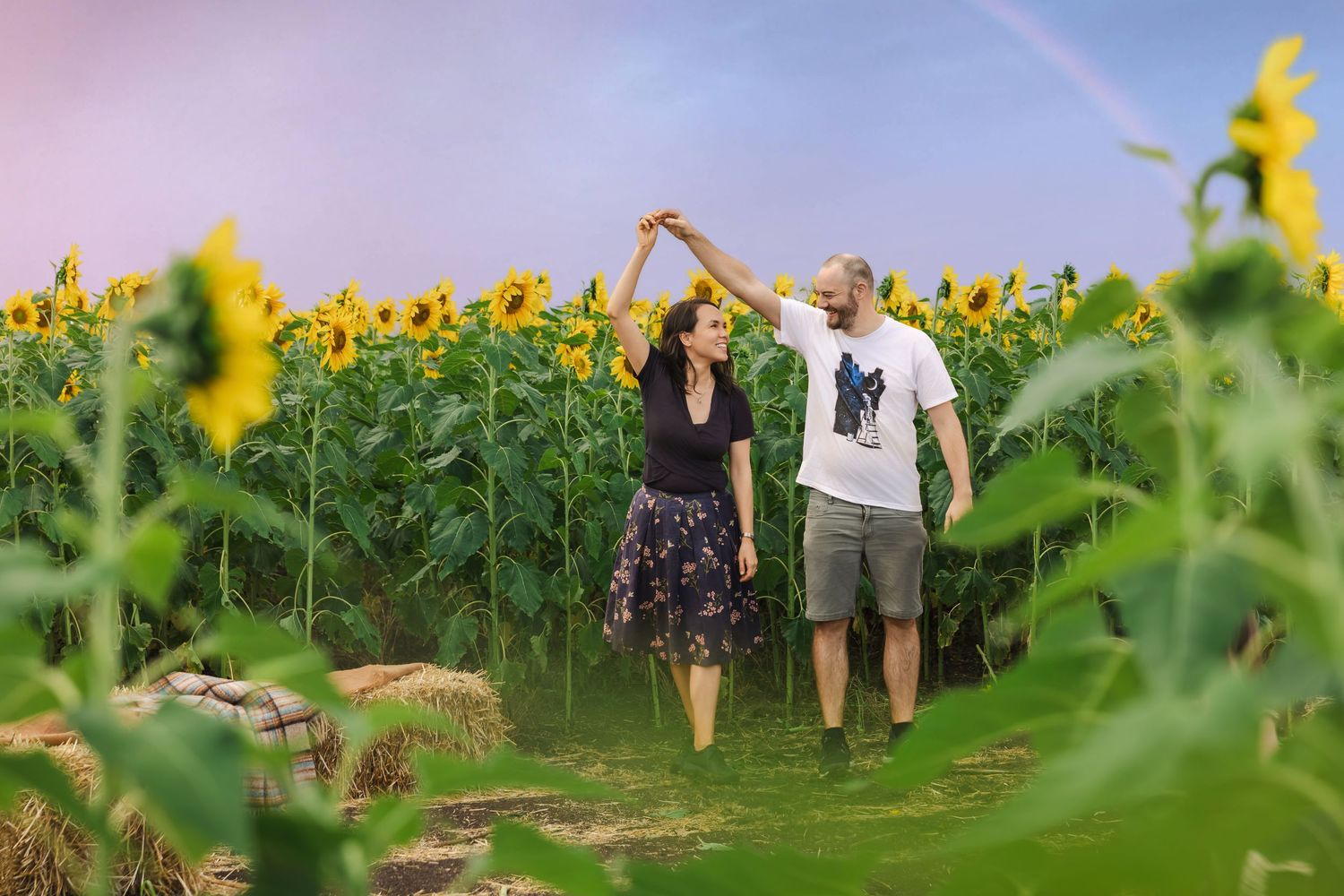Couple dancing joyfully in a colorful sunflower field at sunset.