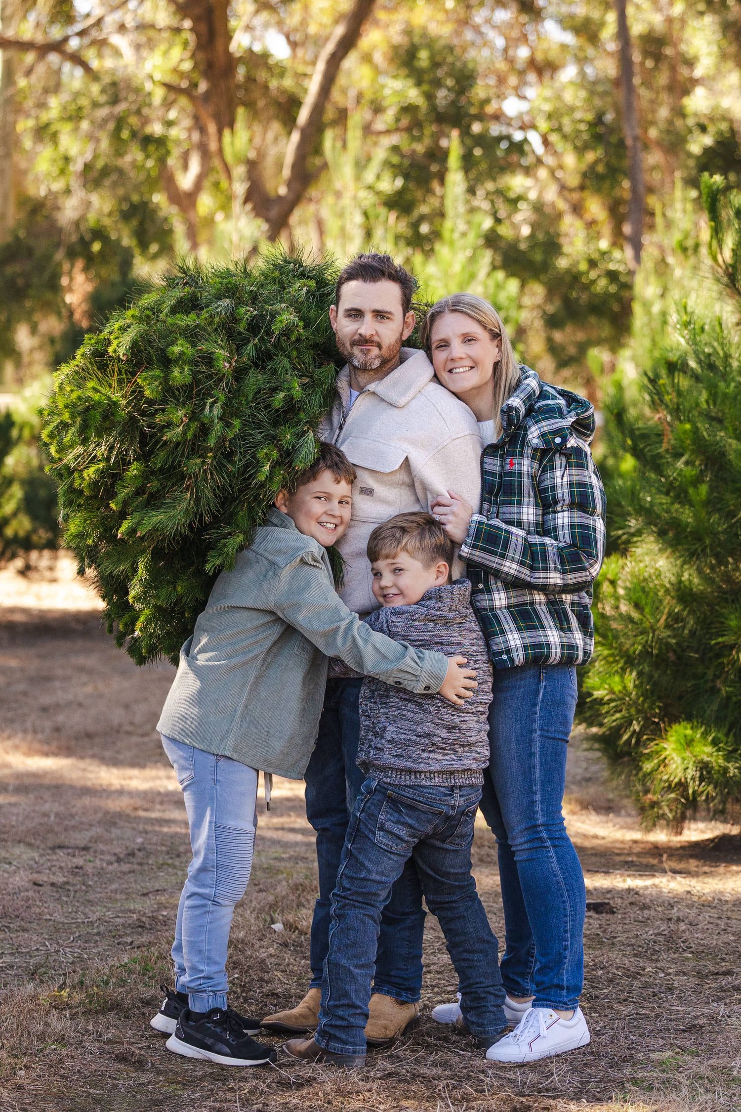 Four candid photos showing playful interaction between family members at a Christmas tree farm with evergreens in background.