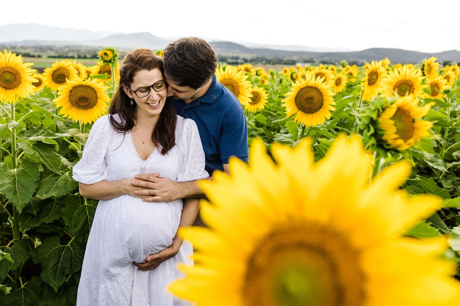 A couple embraces in a vibrant field of tall sunflowers on a summer day in the countryside.