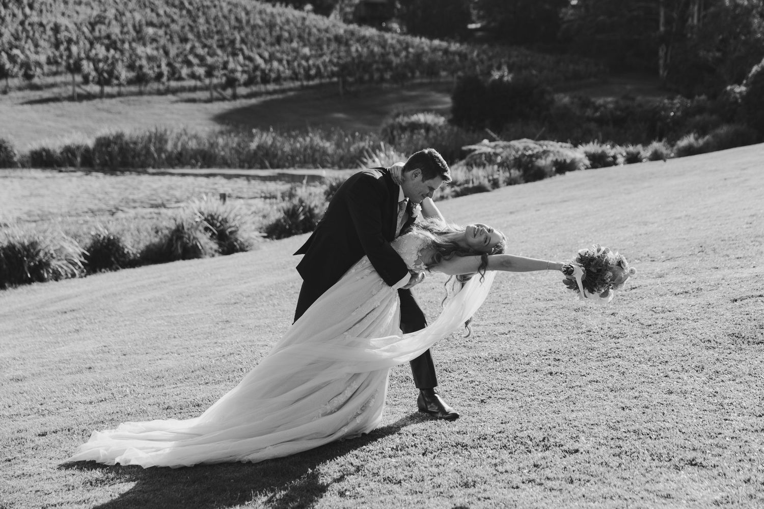 A couple dips dramatically while dancing on a grassy hill.