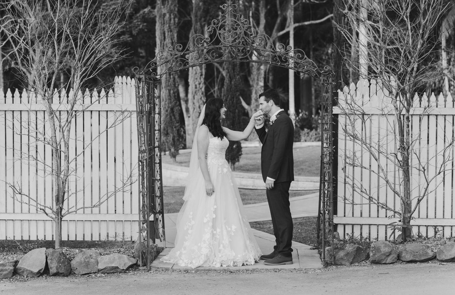 Black and white wedding photos captured against a white picket fence and bare winter trees.