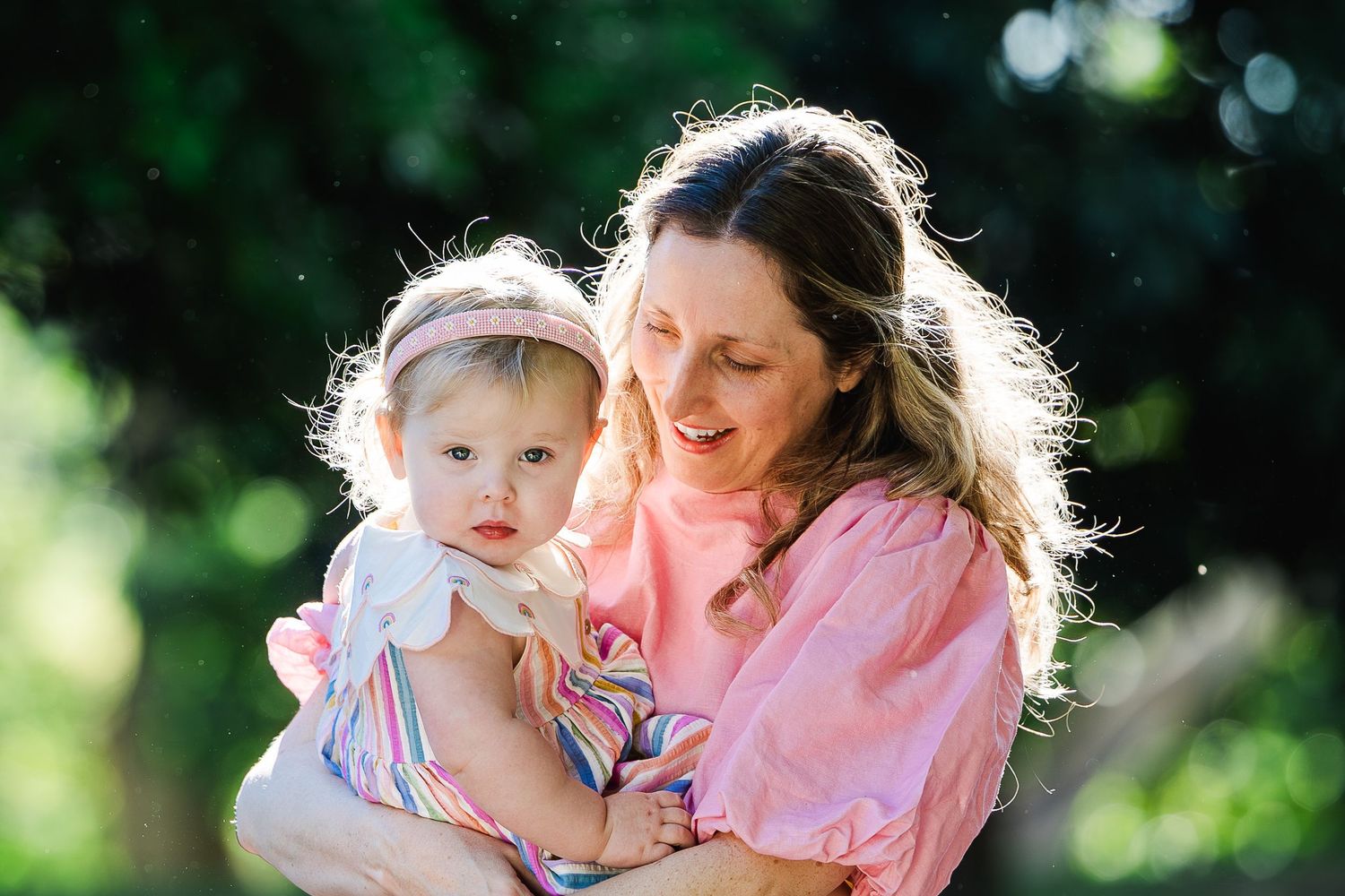 A tender moment shared between parent and child outdoors with sunlit bokeh in the background.